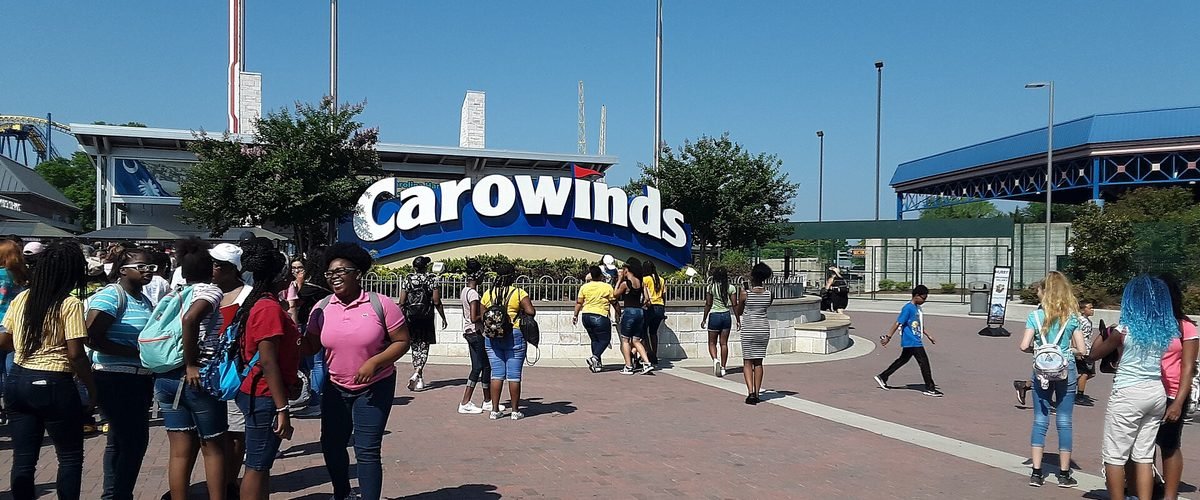 Visitors walking beneath the Carowinds entrance sign on a sunny day