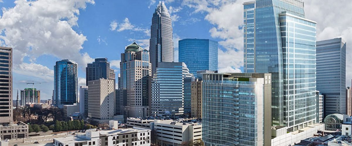 Uptown Charlotte skyline on a clear day, with modern glass towers and scattered clouds
