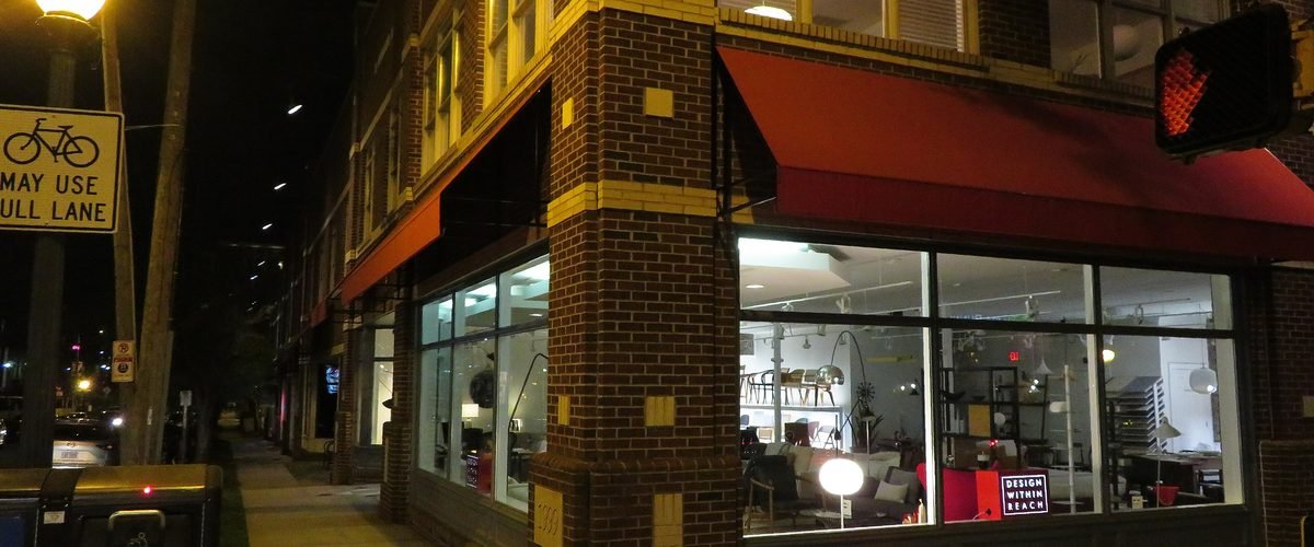 Nighttime street corner in South End, Charlotte, with a lit storefront and brick mill-style architecture